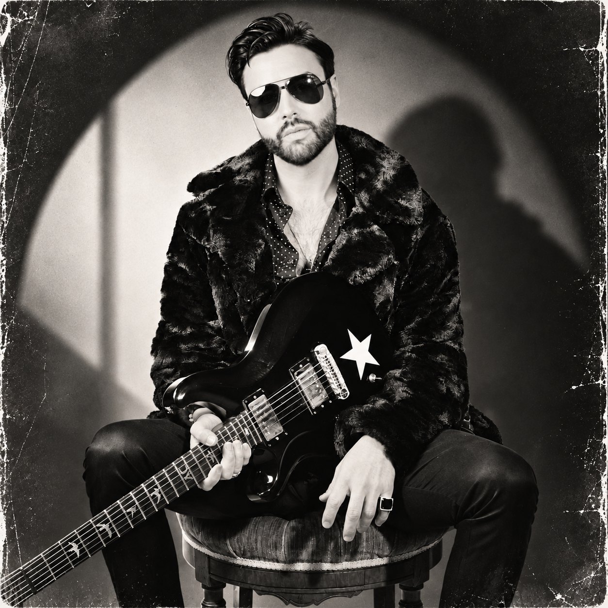 ADOM singer songwriter seated with an electric guitar, wearing a fur coat and sunglasses.